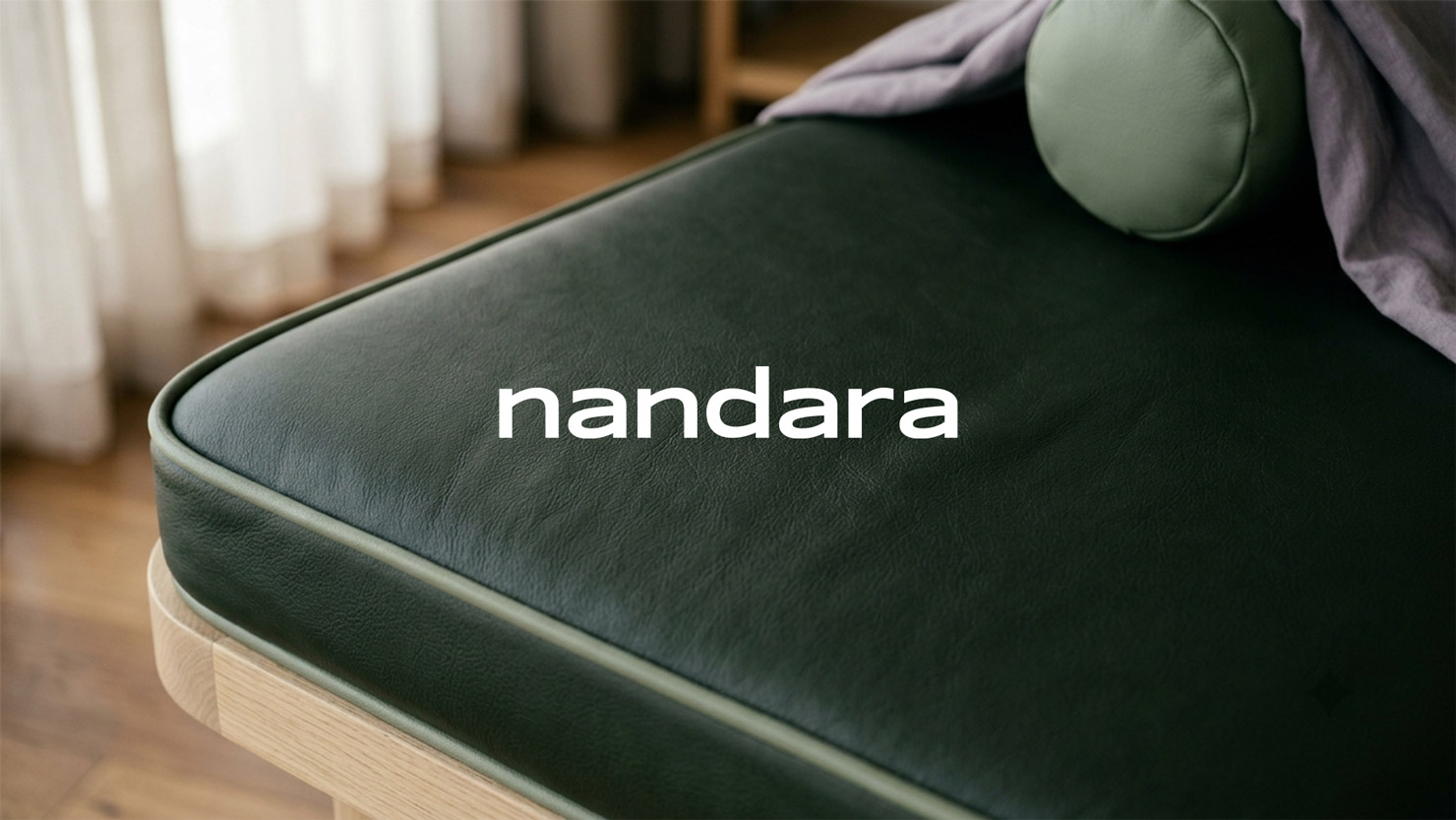 Nandara wordmark on a dark green massage table with sage piping